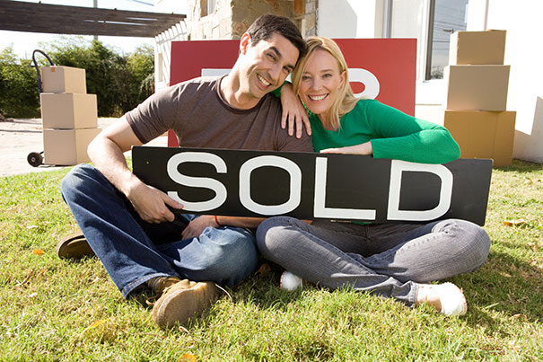 couple with sold sign in front of new home
